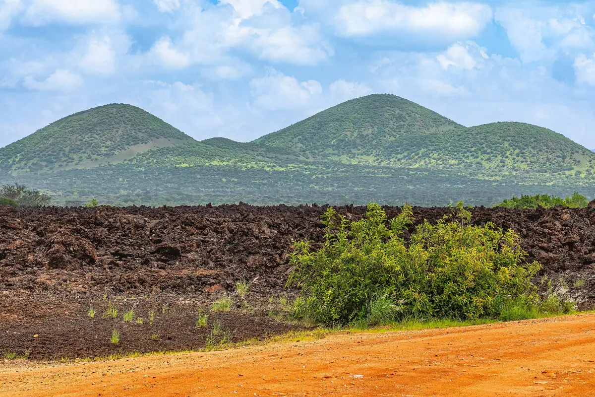 Dark Shetani lava field below green rounded Chyulu Hills in Tsavo West