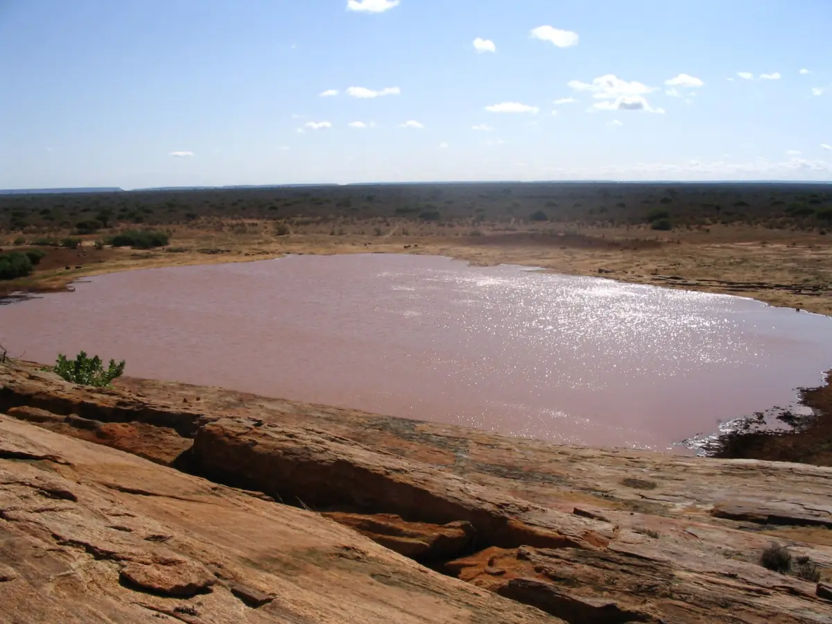 Water pool below the red rock face of Mudanda Rock in Tsavo East